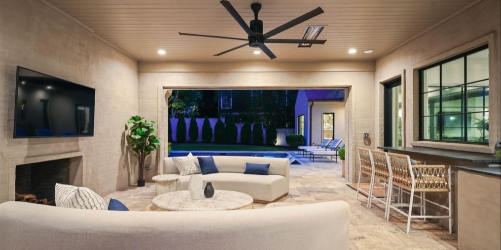 Covered outdoor living room with television and pool view at night