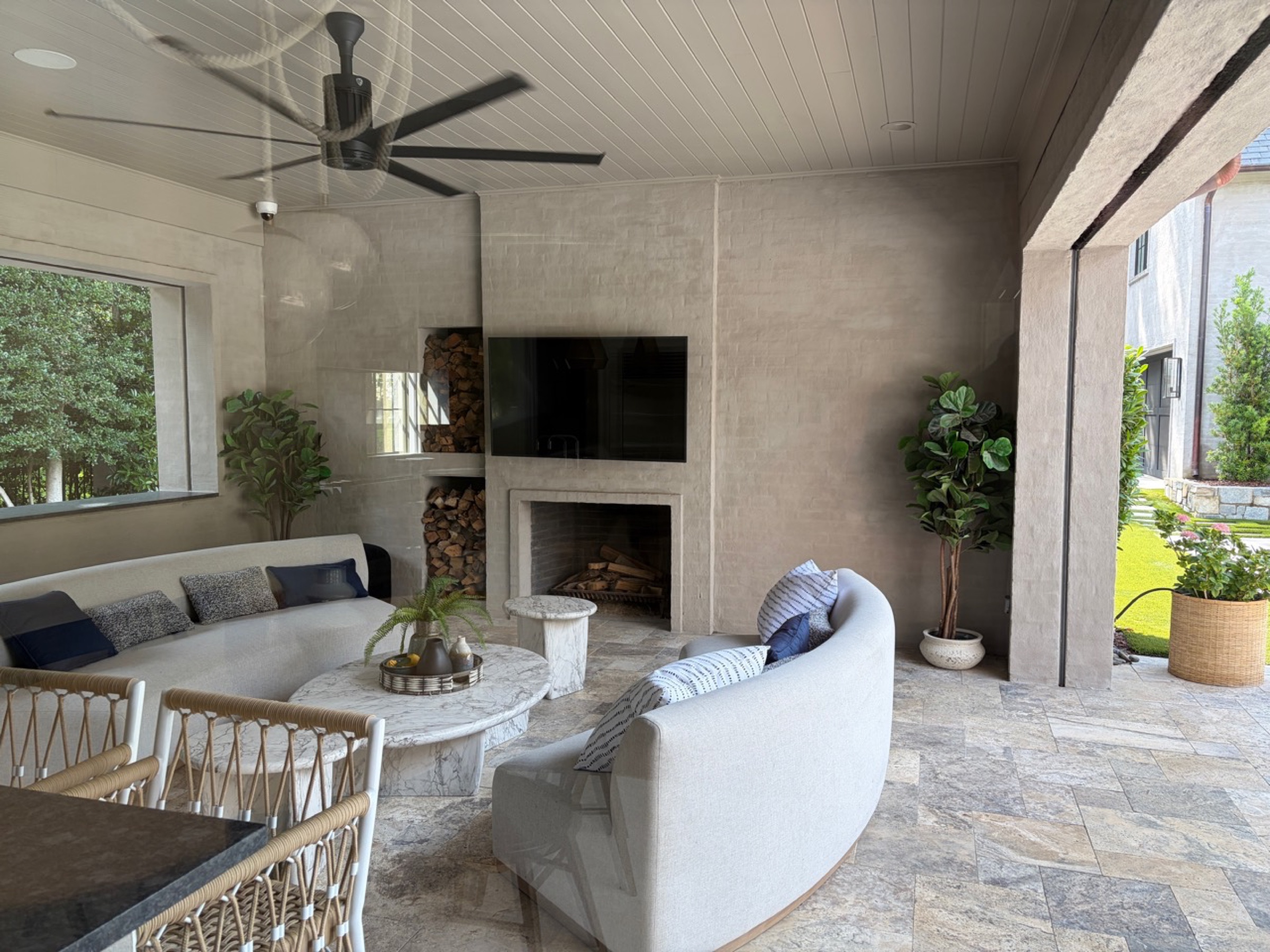 Covered outdoor living room with television, fireplace, ceiling fan, and speakers